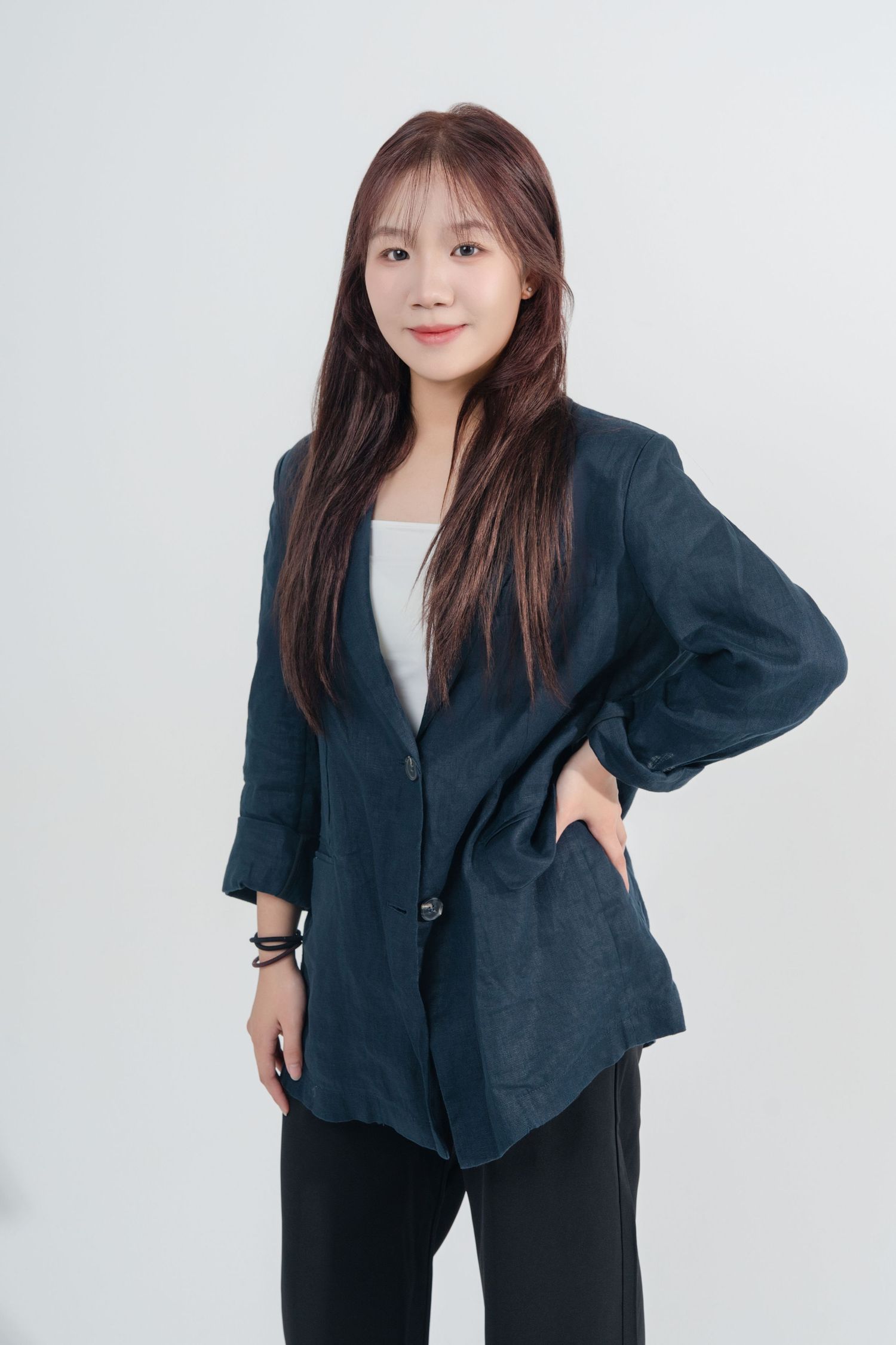 Professional portrait of someone wearing a navy blazer over white top with black pants against light background.