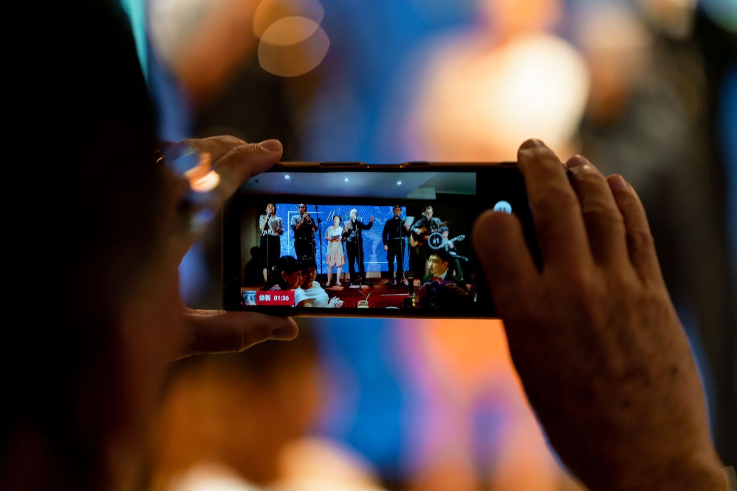 Someone captures a performance on their smartphone at an evening event.
