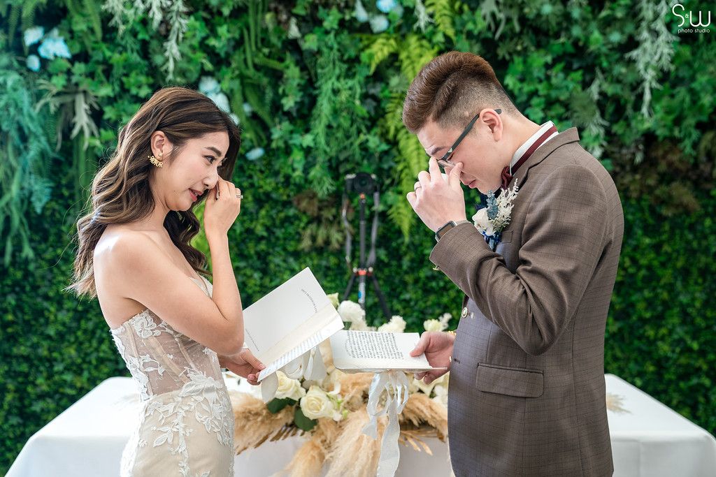 Couple becomes emotional while reading their wedding vows in front of a green wall.