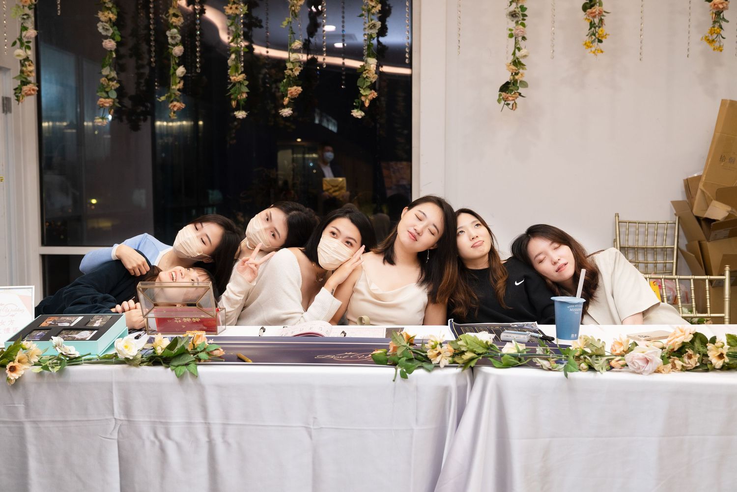 A group relaxes together at a decorated table with floral arrangements and hanging decor in a bright indoor setting.