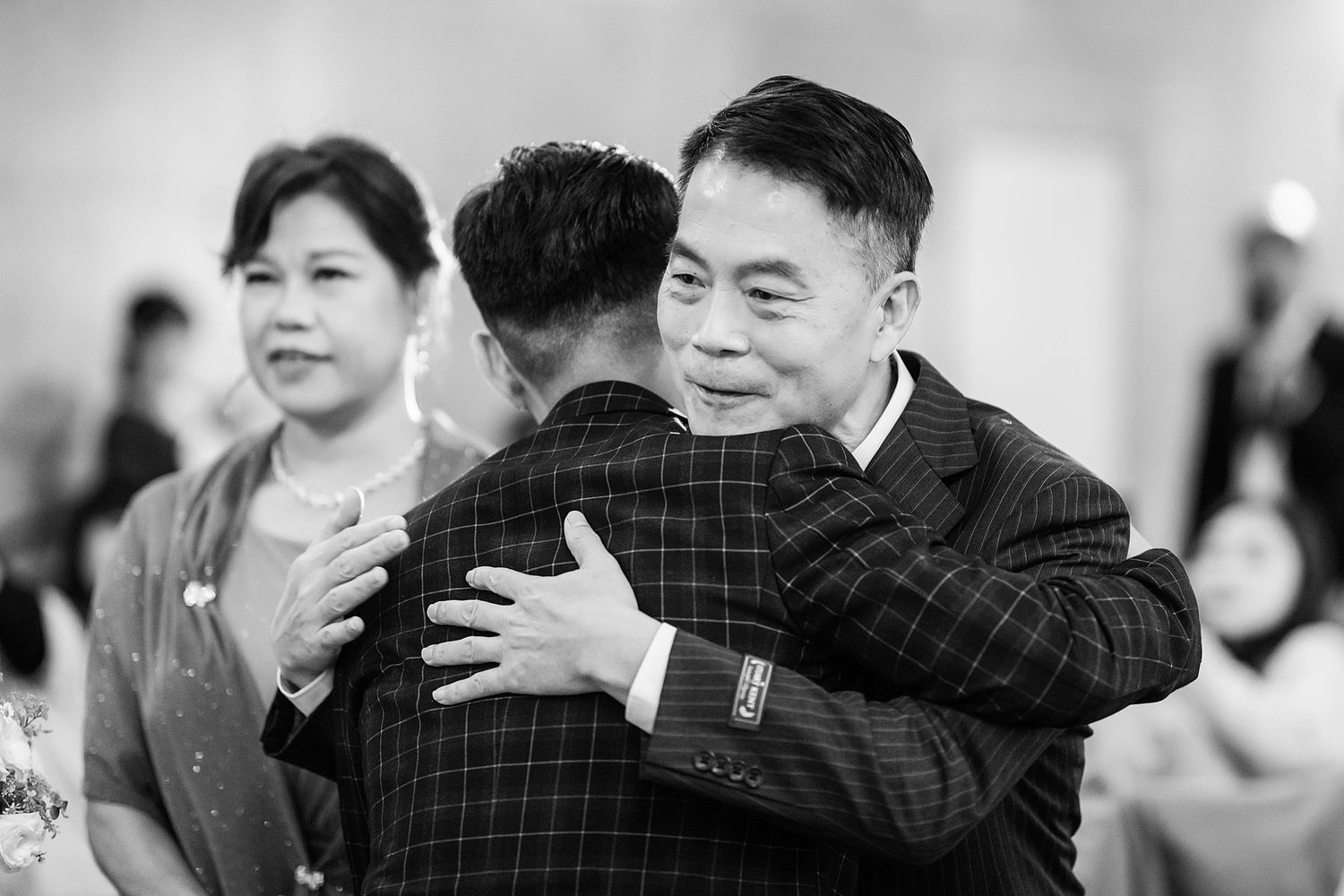 A candid black and white shot showing warm embraces and smiles during what appears to be a social gathering.