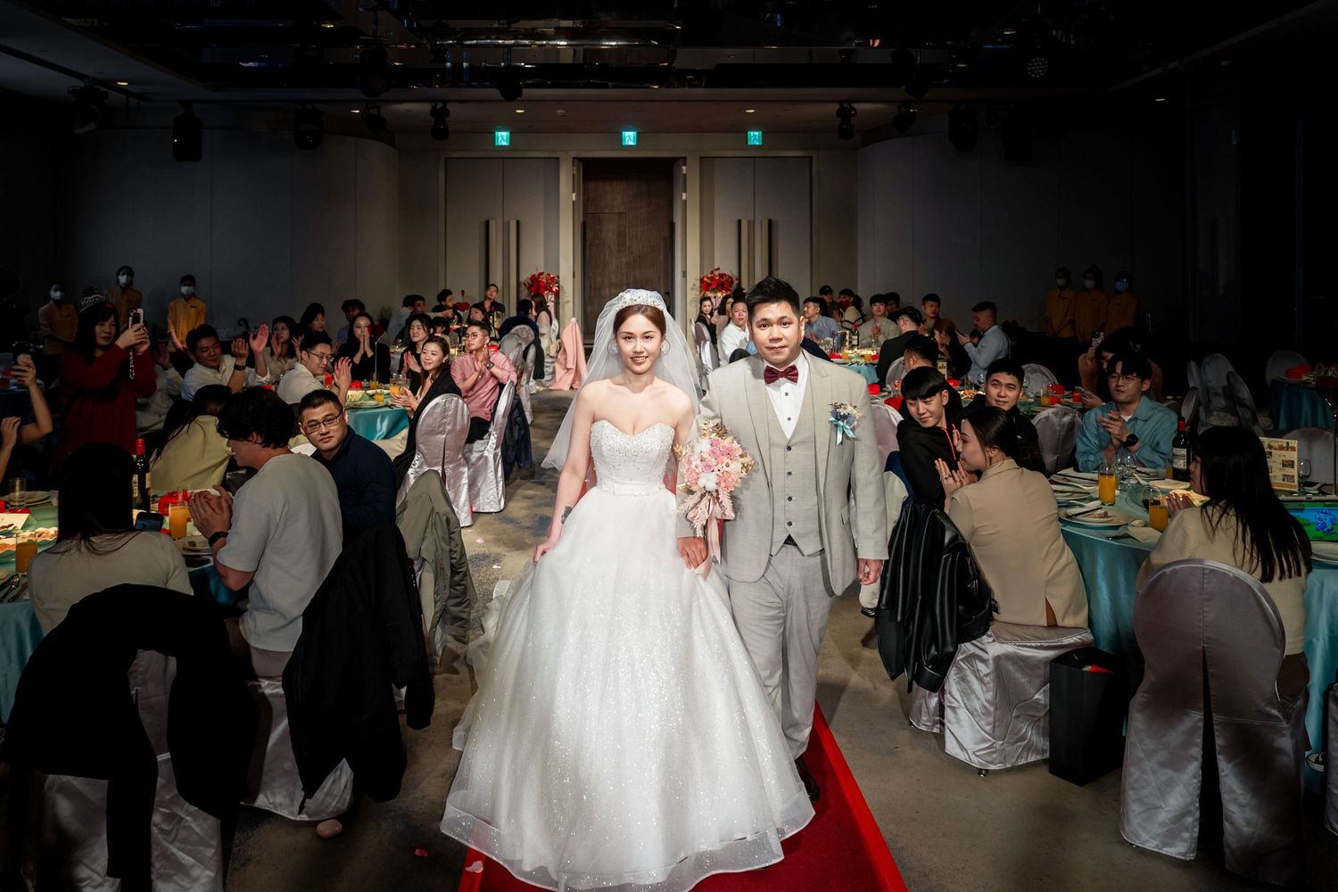 A wedding reception celebration shows guests mingling and dancing in a large banquet hall.