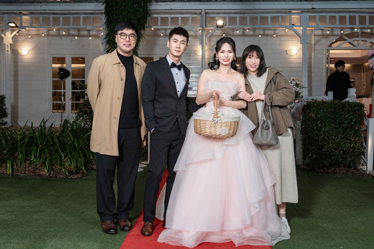 Wedding party poses outdoors at an elegant venue with string lights and greenery in the background.