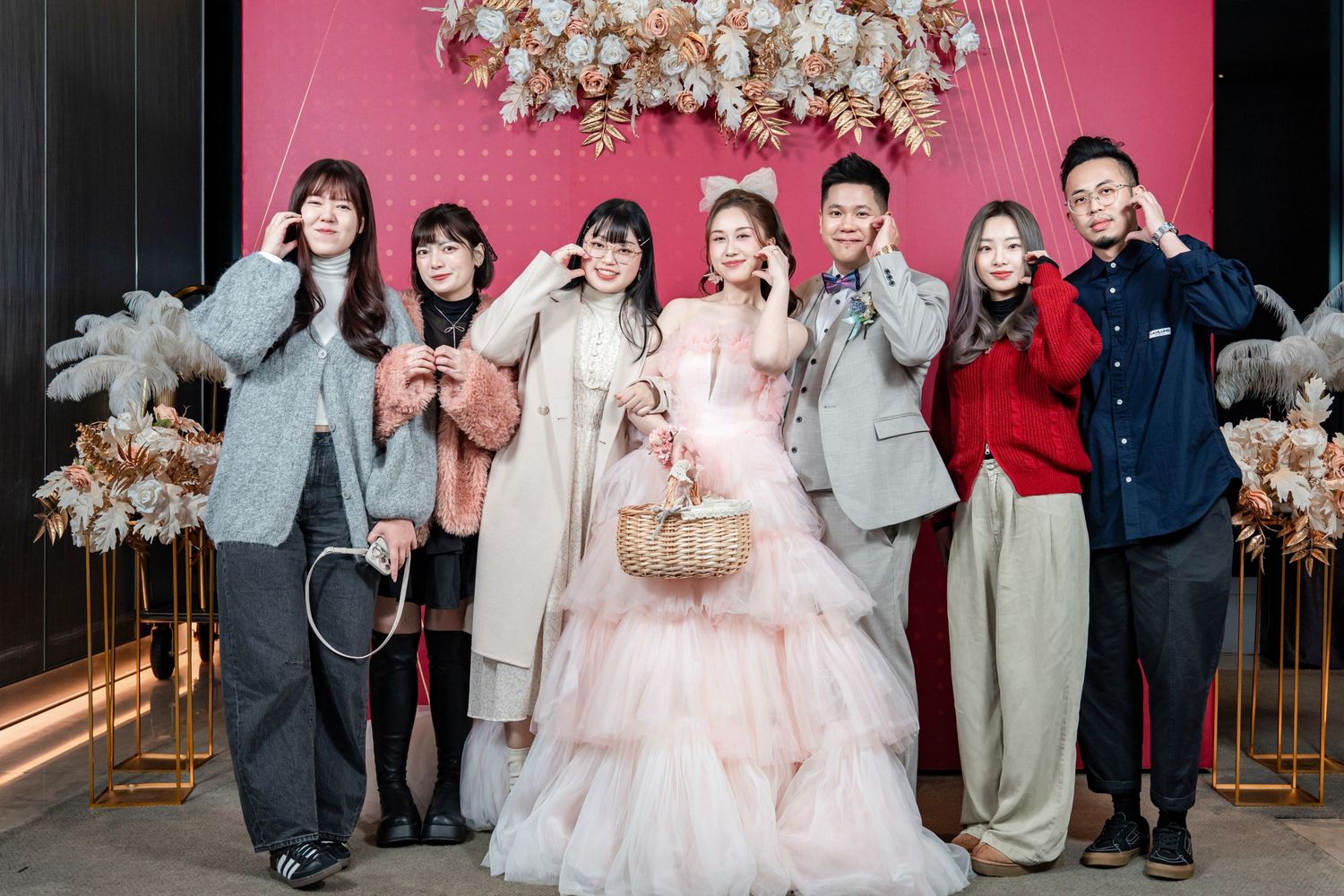 Festive gathering of people posing against bright pink backdrop with white floral decorations.