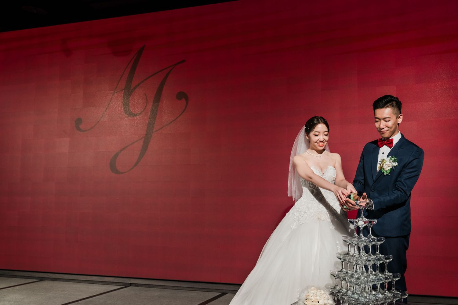A newlywed couple shares a joyful moment together against a red wall with elegant monogram lettering.