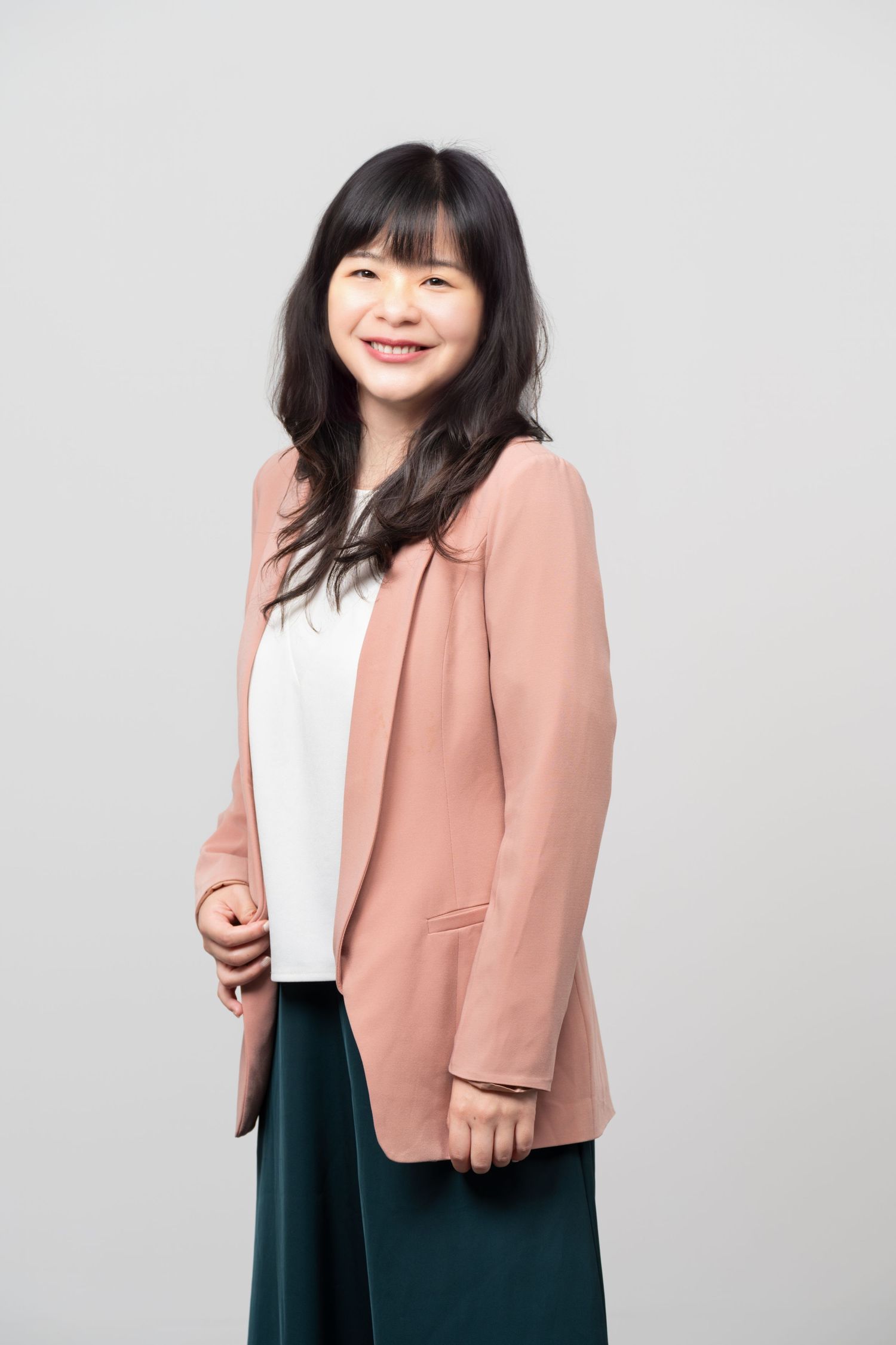 Professional studio portrait of someone in a peach blazer, white top and teal skirt against a gray background.