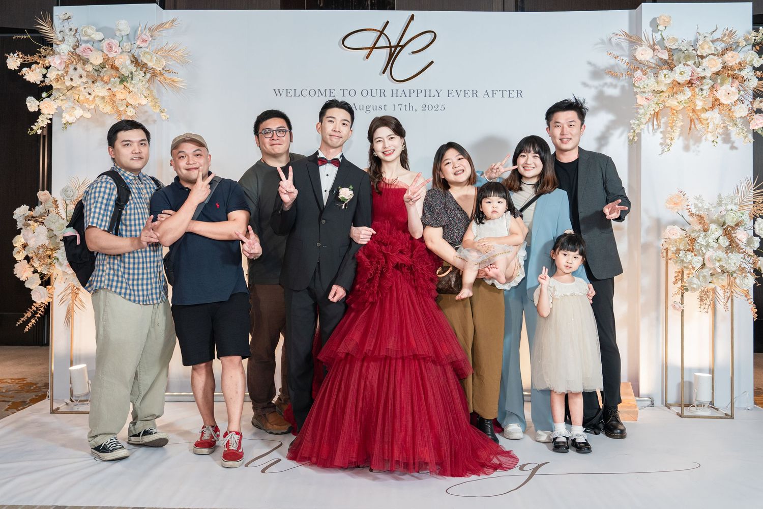 Elegant wedding celebration with burgundy ball gown and formal attire in a luxurious white and floral decorated venue.