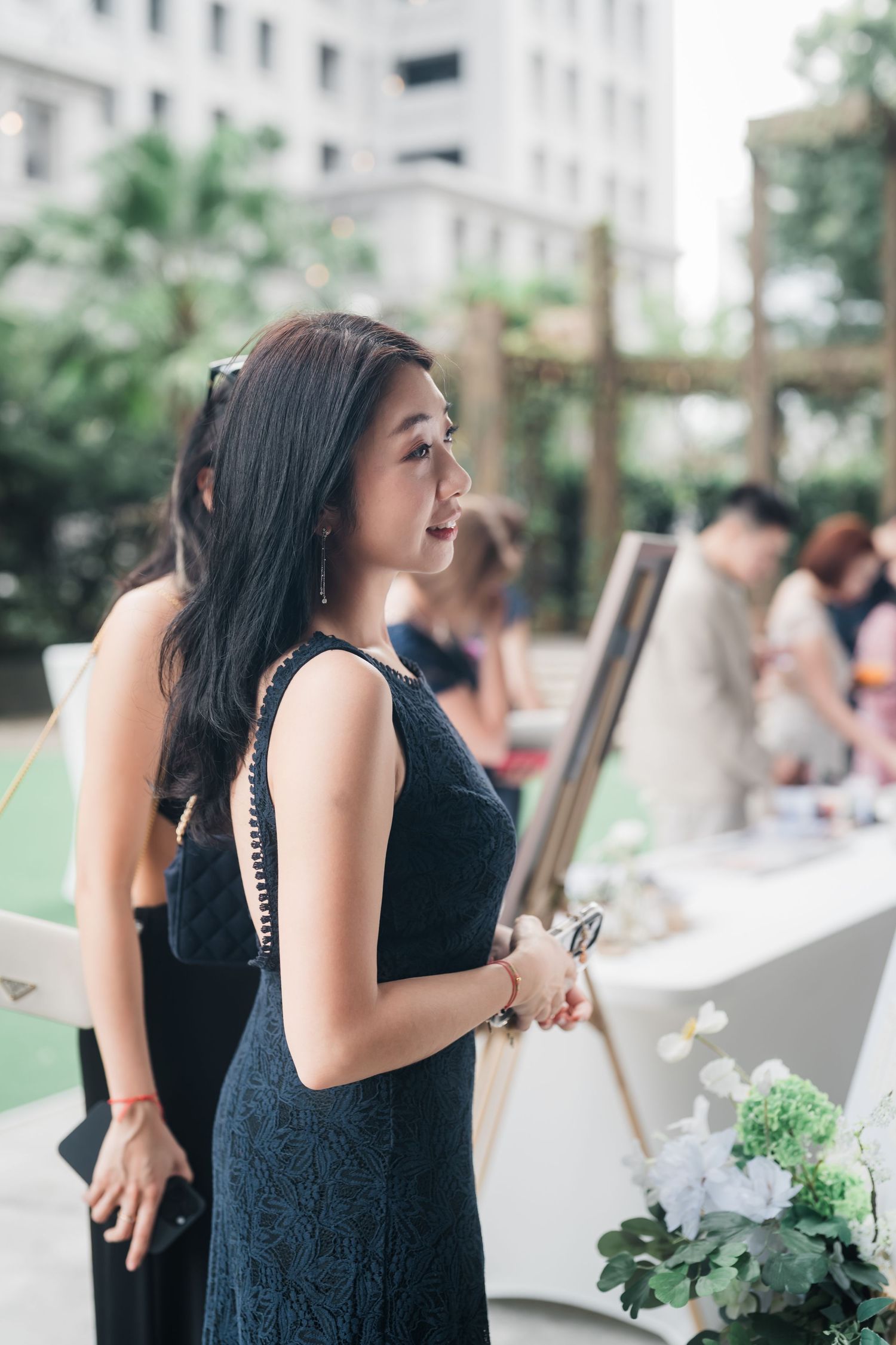 A guest in a dark blue sleeveless dress laughs during an outdoor garden party reception.