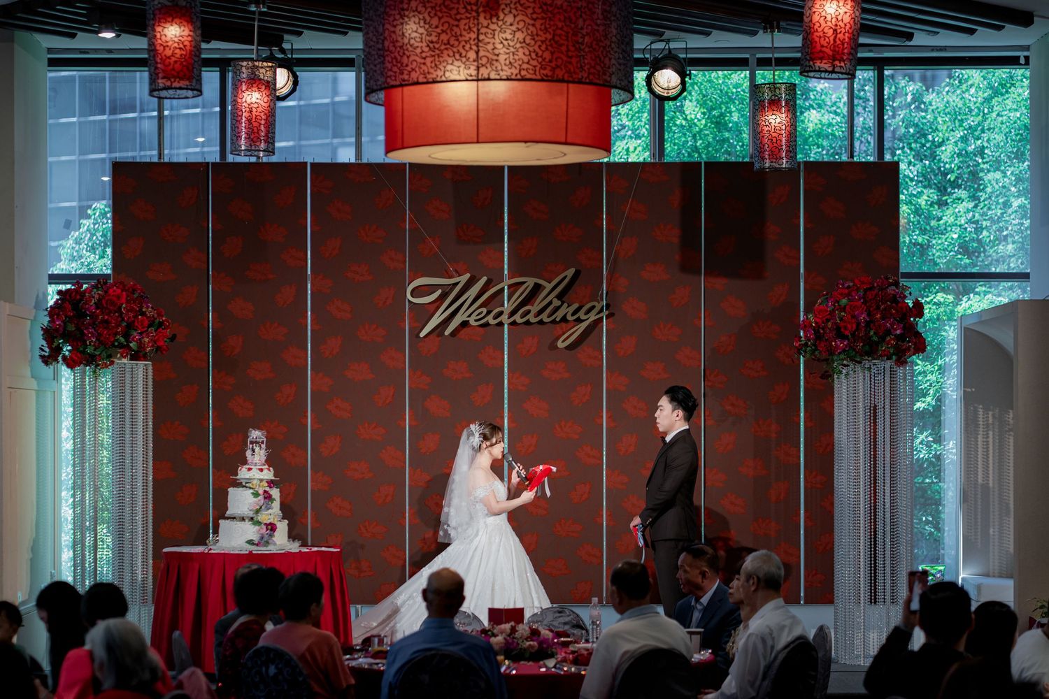 A wedding ceremony in a modern venue with red lighting, featuring a couple at the altar and a wedding cake display.