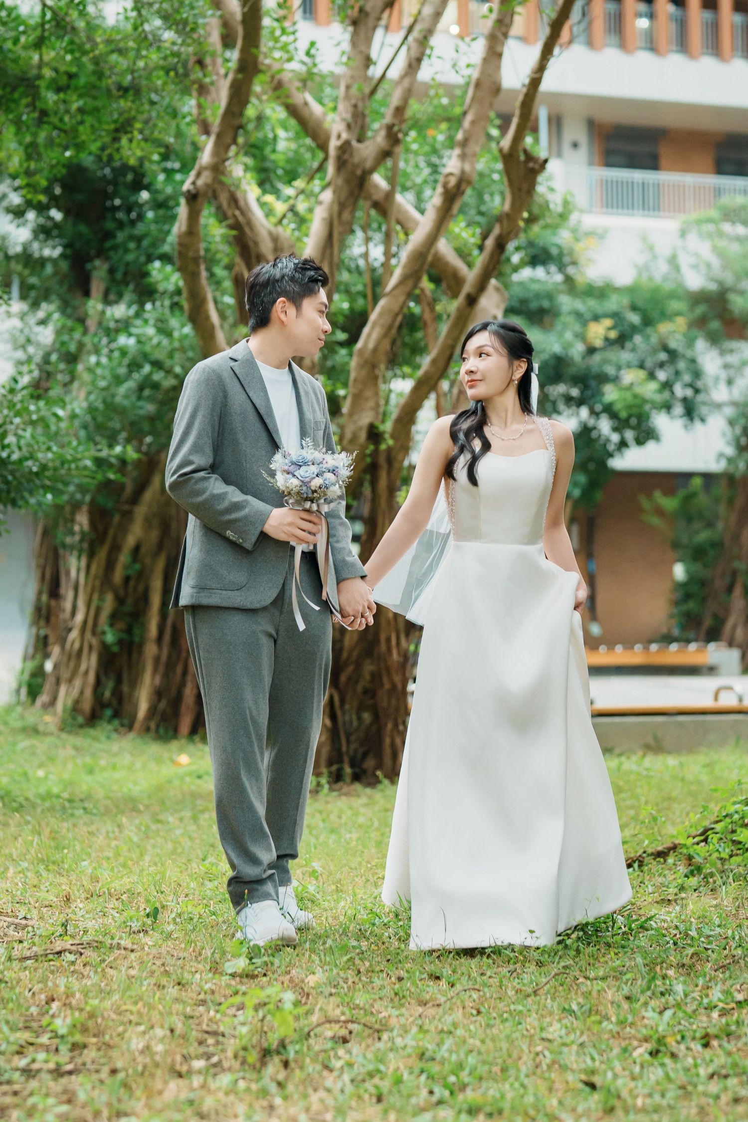 A couple shares a romantic moment in a garden setting wearing wedding attire with lush greenery surrounding them.