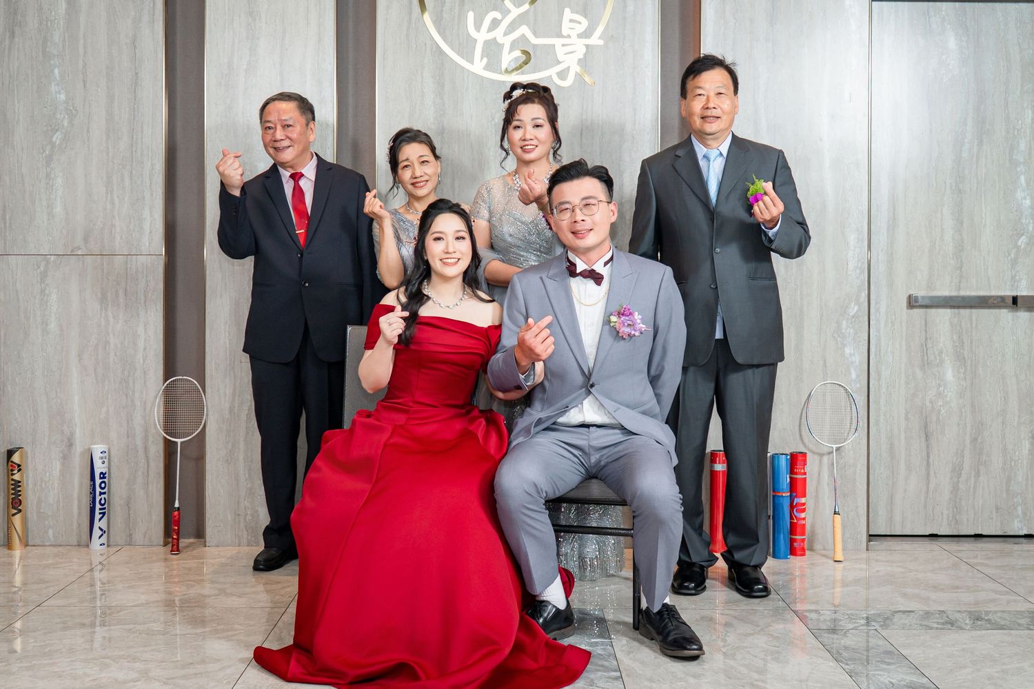 Wedding party poses together in modern indoor venue with red accents and grey stone walls.