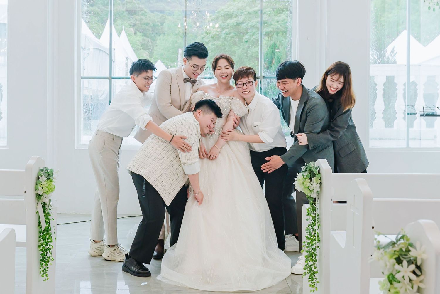 A wedding party poses playfully in a bright white studio space with green floral decorations.