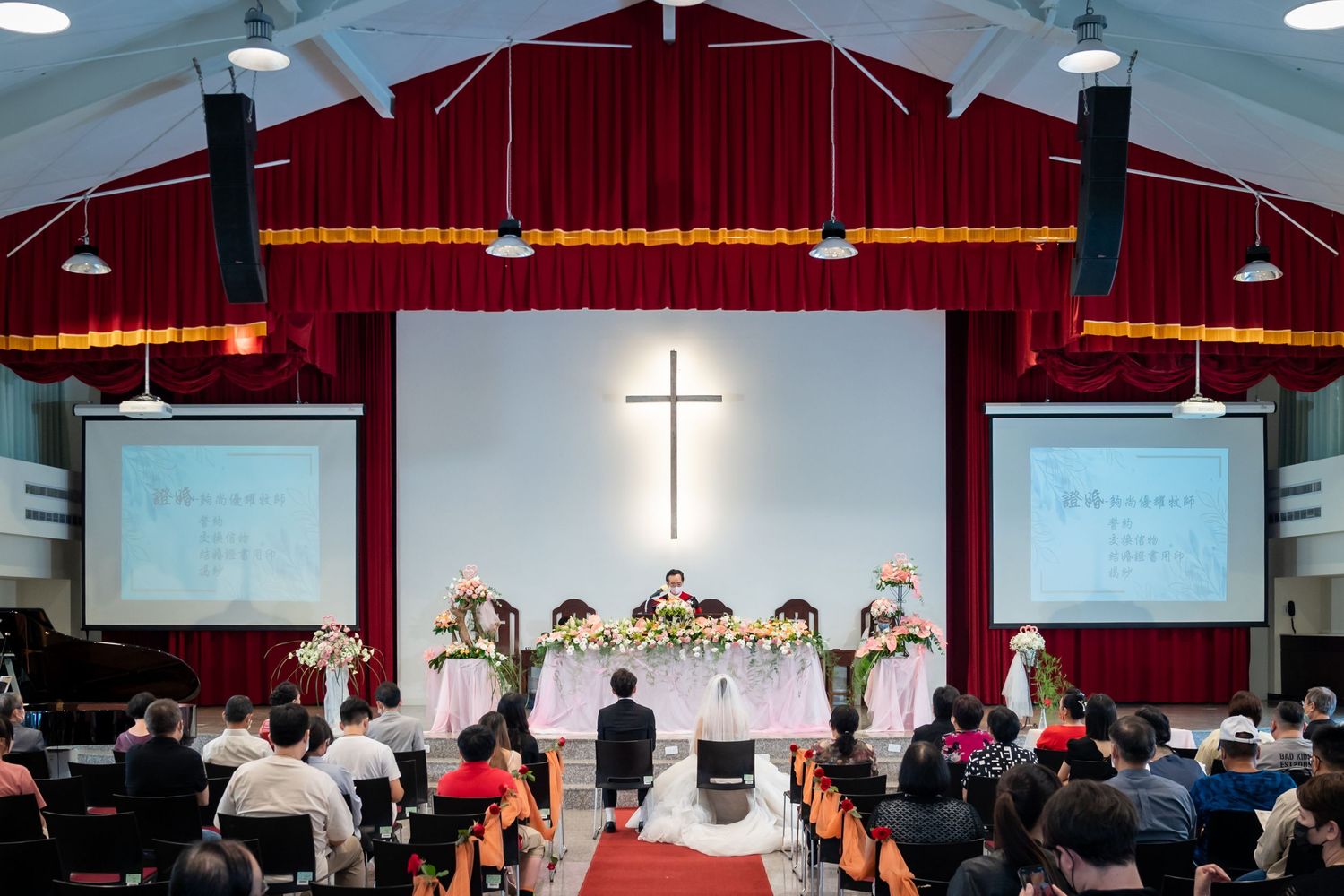 Church wedding venue with illuminated cross and red curtains during ceremony.