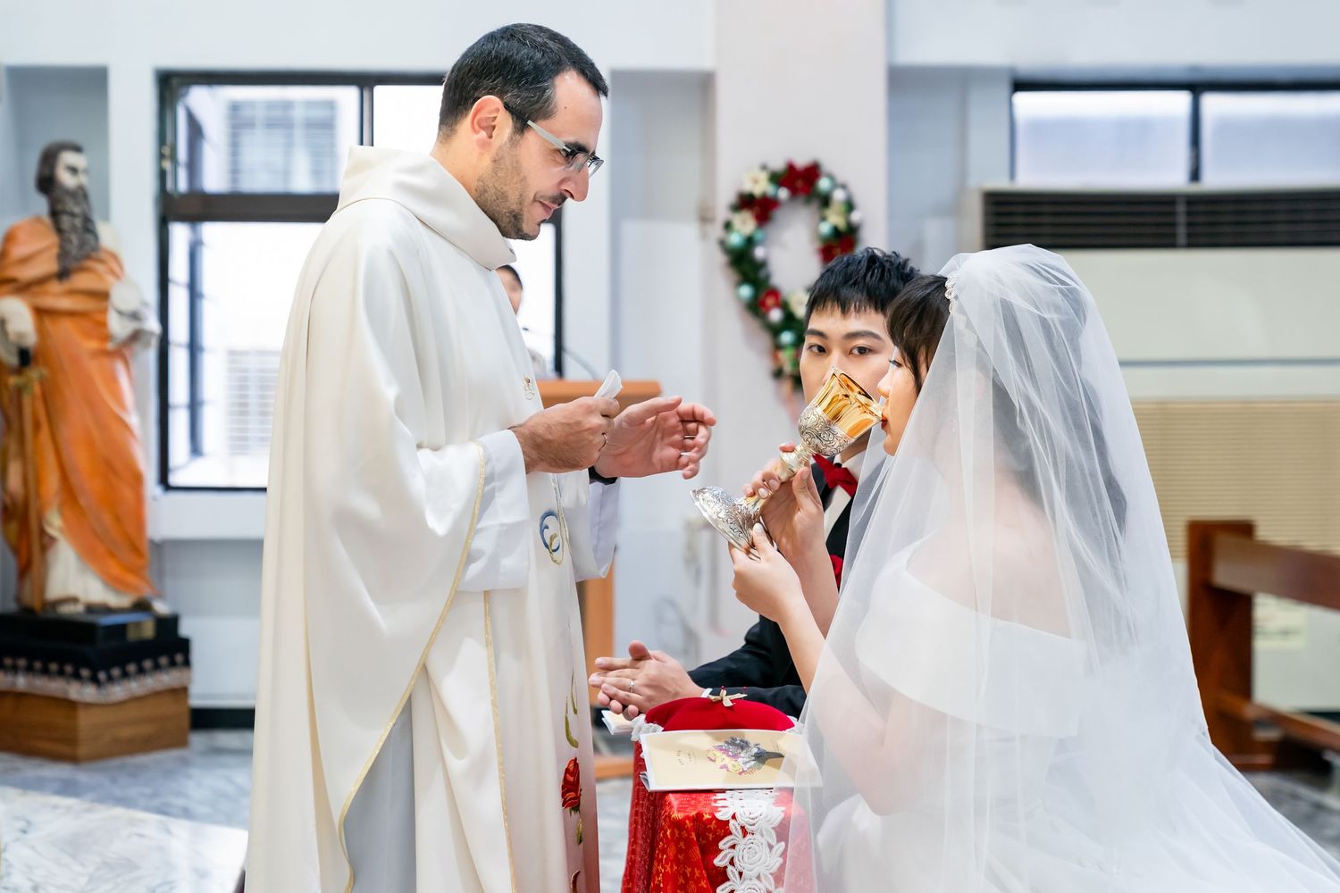 Priest performing communion ritual during wedding ceremony at decorated church altar.