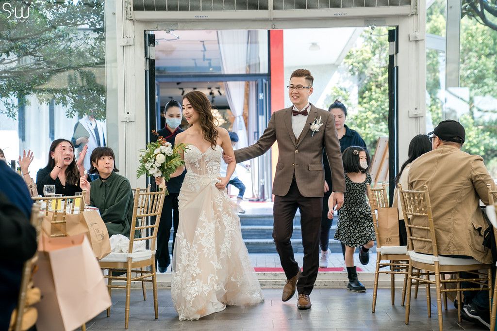 Wedding ceremony entrance with couple walking down aisle in elegant venue with guests seated on gold chairs.
