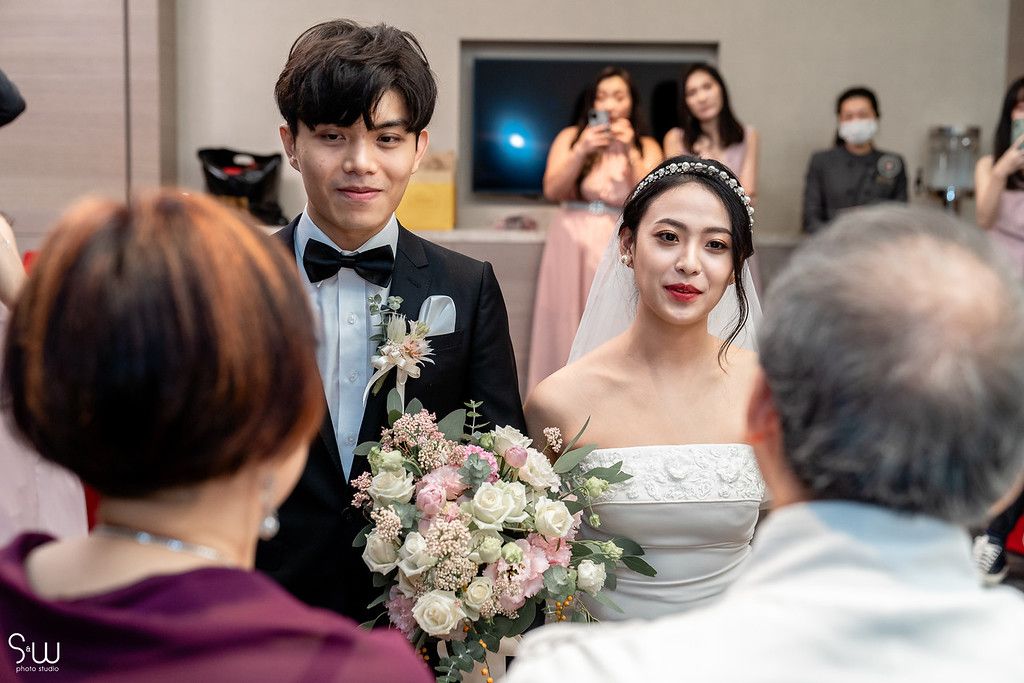 A wedding couple holding a pink floral bouquet while greeting guests at their reception.