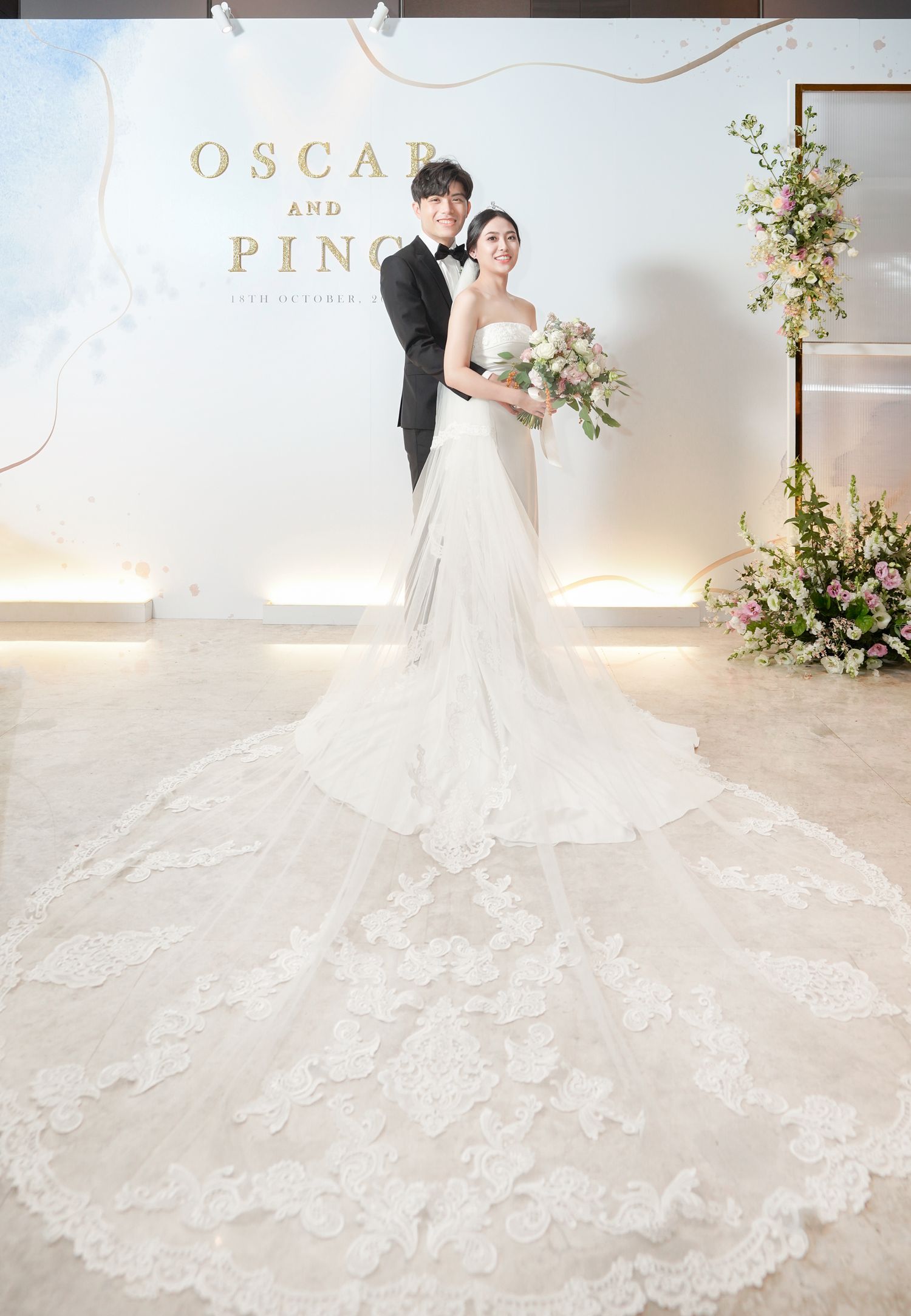 Wedding portrait in front of decorative backdrop showcasing bride's elaborate lace train.