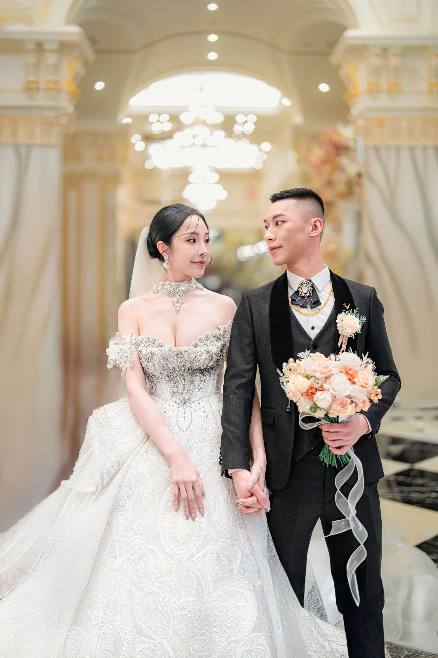 Elegant wedding couple shares romantic moments in a luxurious ballroom with ornate decor and soft lighting.