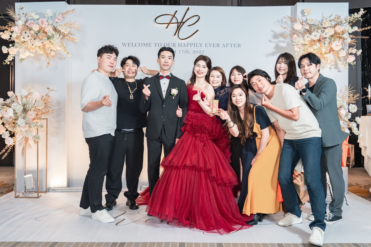 Formal celebration with a group in evening attire posing together at an elegantly decorated venue with floral arrangements.