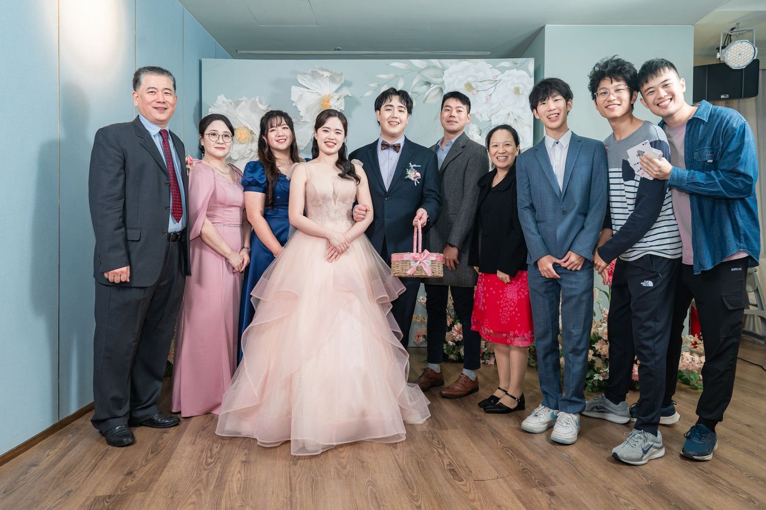 A group of formally dressed people gather together for a wedding photo in a hallway.