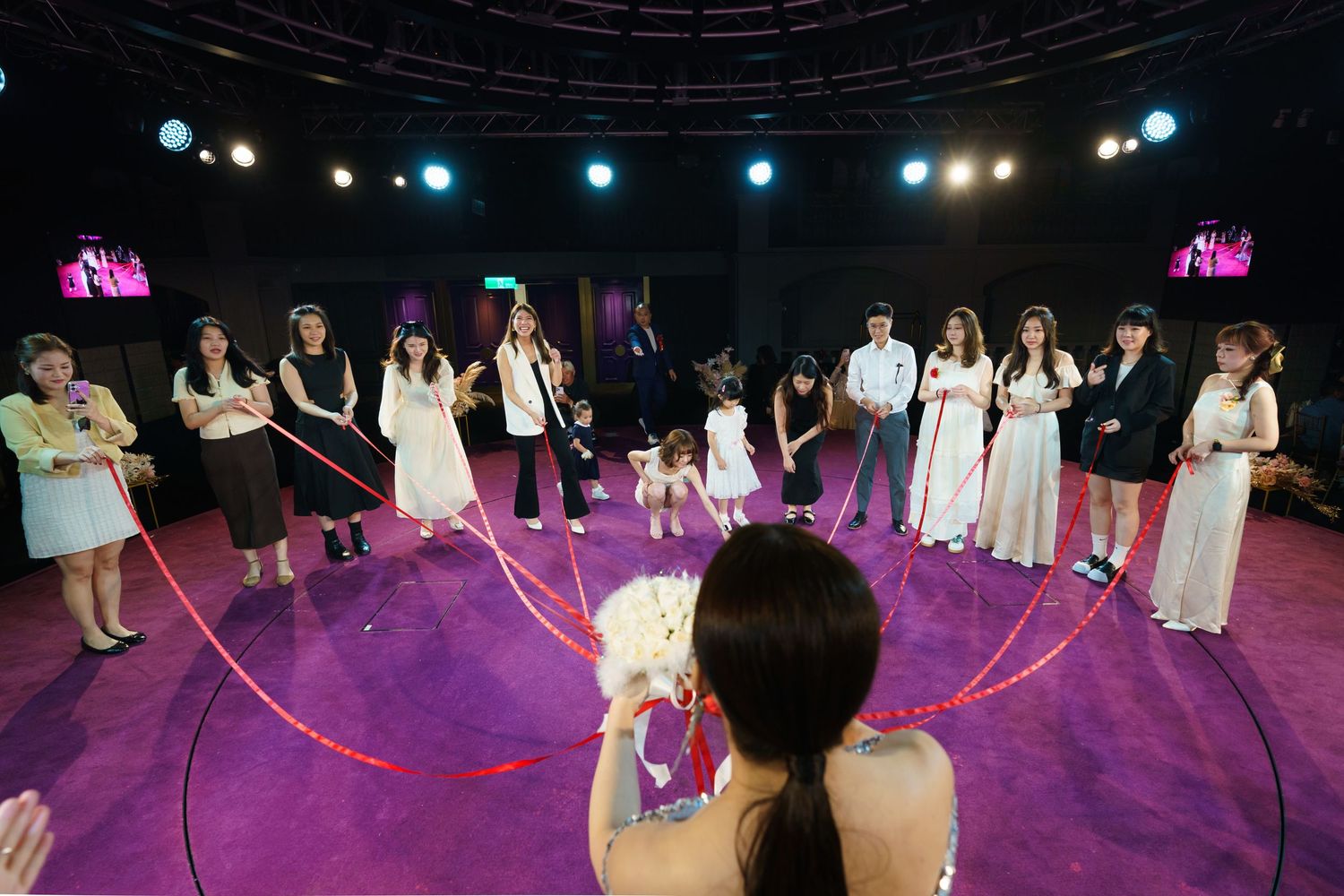 Performers stand in a circle on a purple-lit stage during a theatrical performance with blue spotlights overhead.