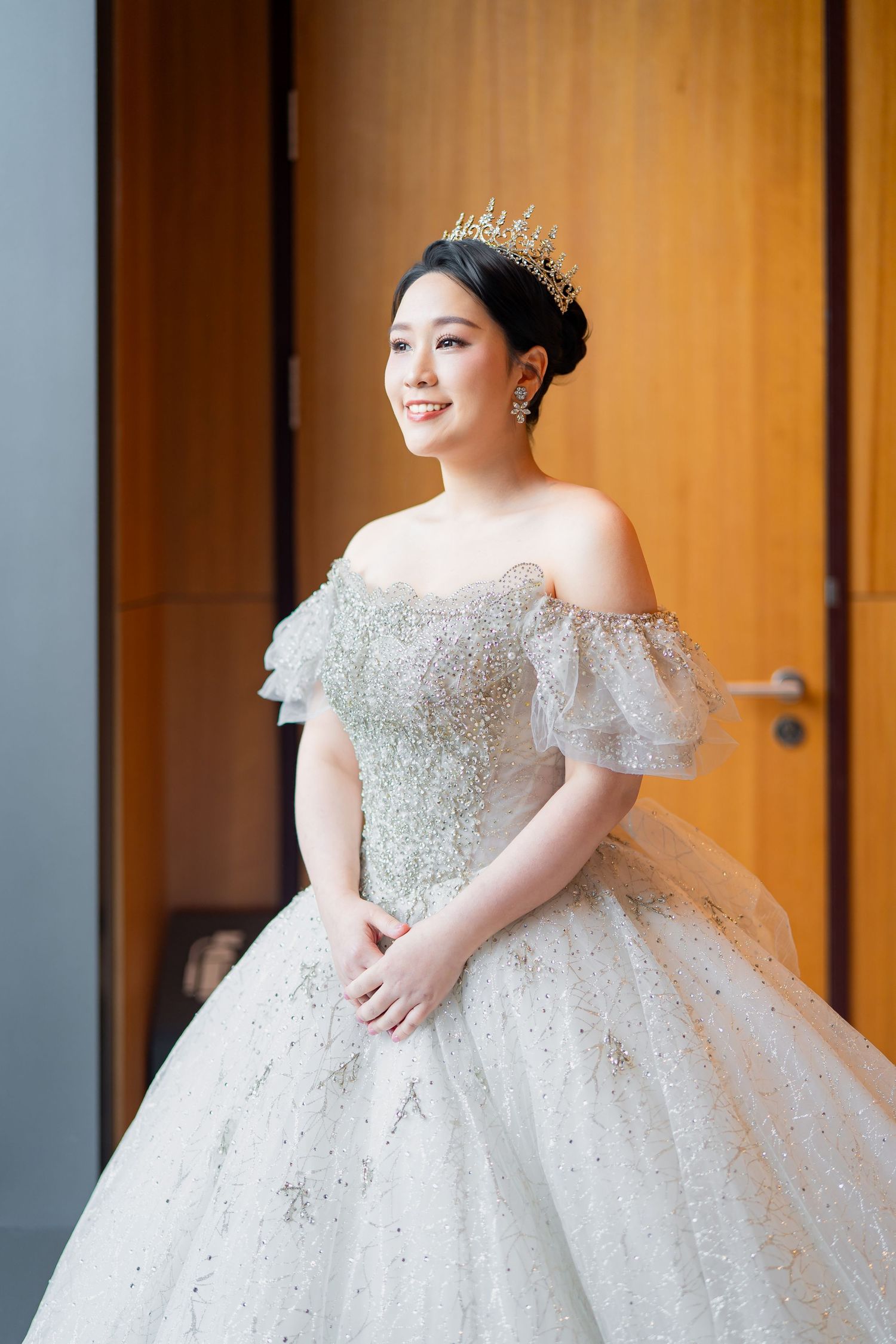 A bride wears a stunning off-shoulder ball gown wedding dress with intricate beading and sparkle details.