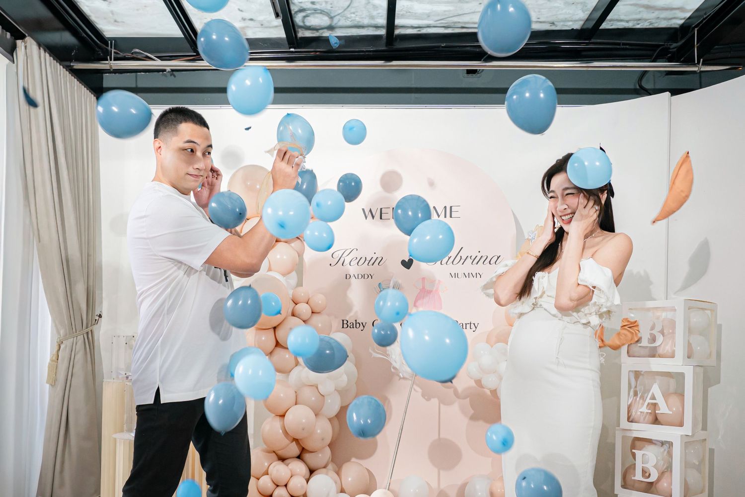 A gender reveal party celebration with blue balloons floating in a bright modern room with white decor.