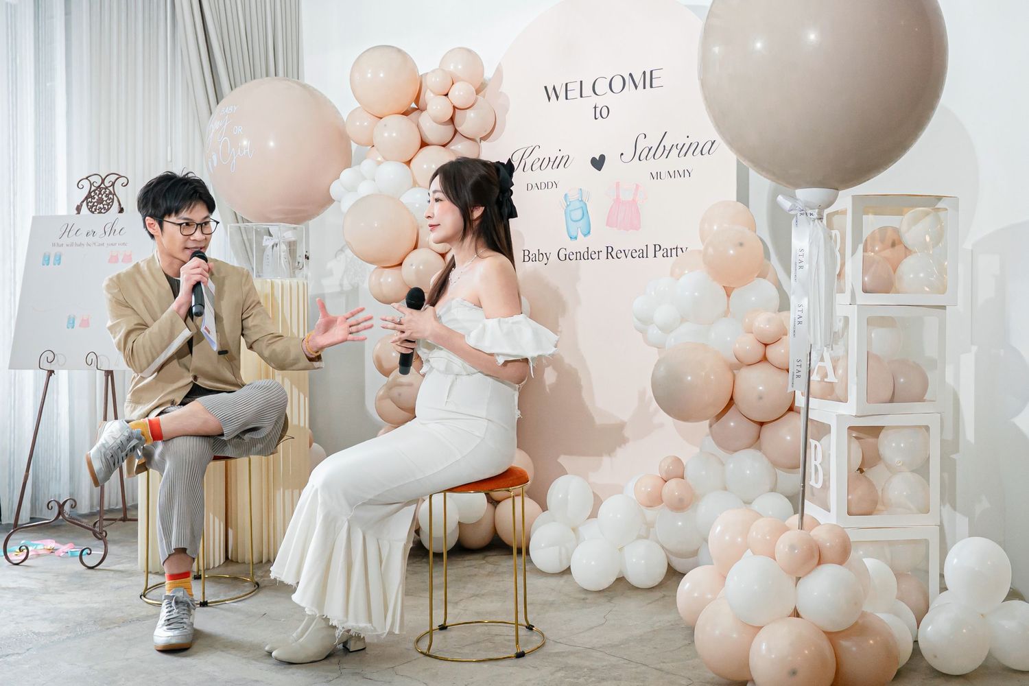 Elegant wedding celebration setup with blush pink balloon arch and white welcome sign against light gray backdrop.