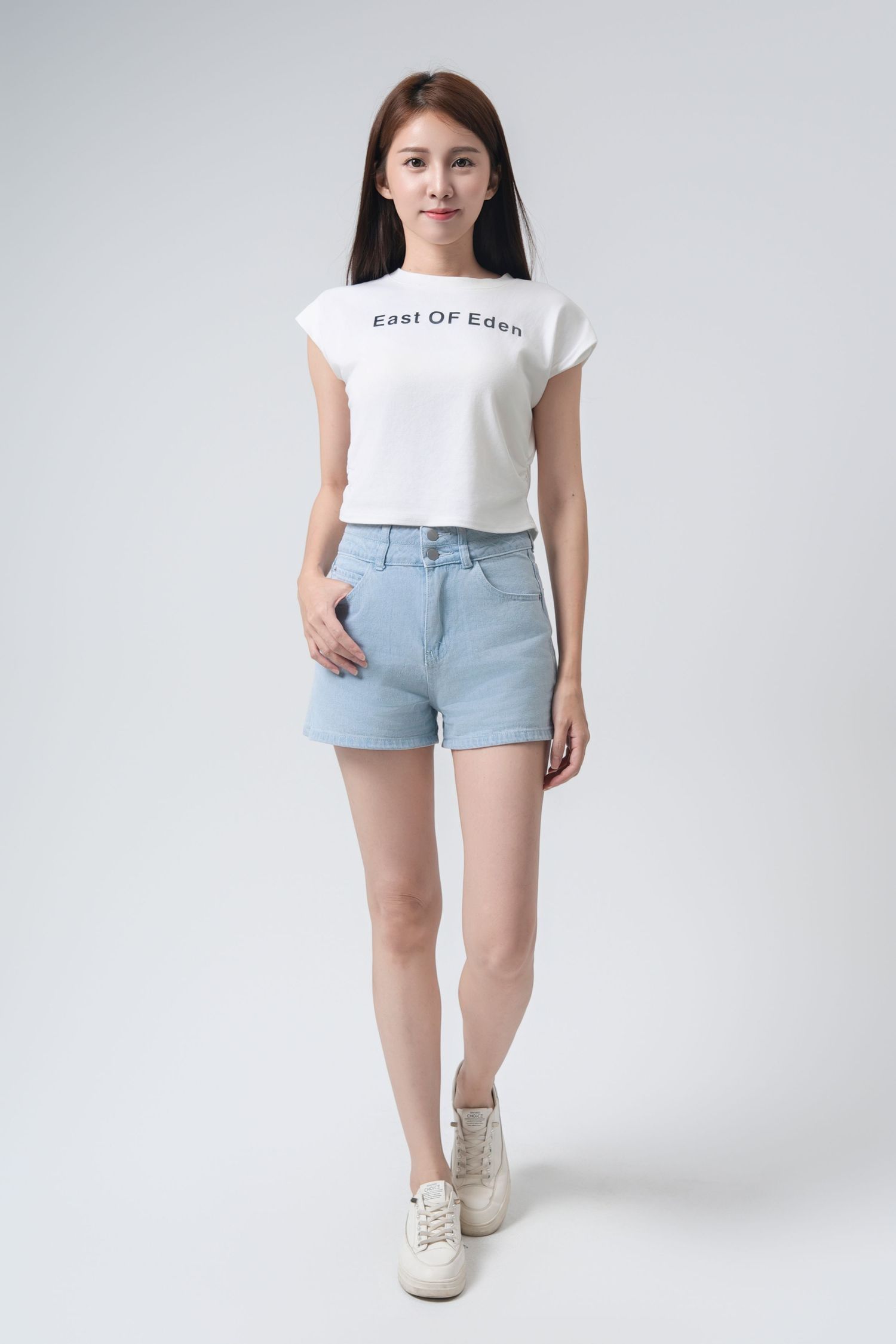 Model wearing light blue denim shorts and white t-shirt with white sneakers against white studio background.