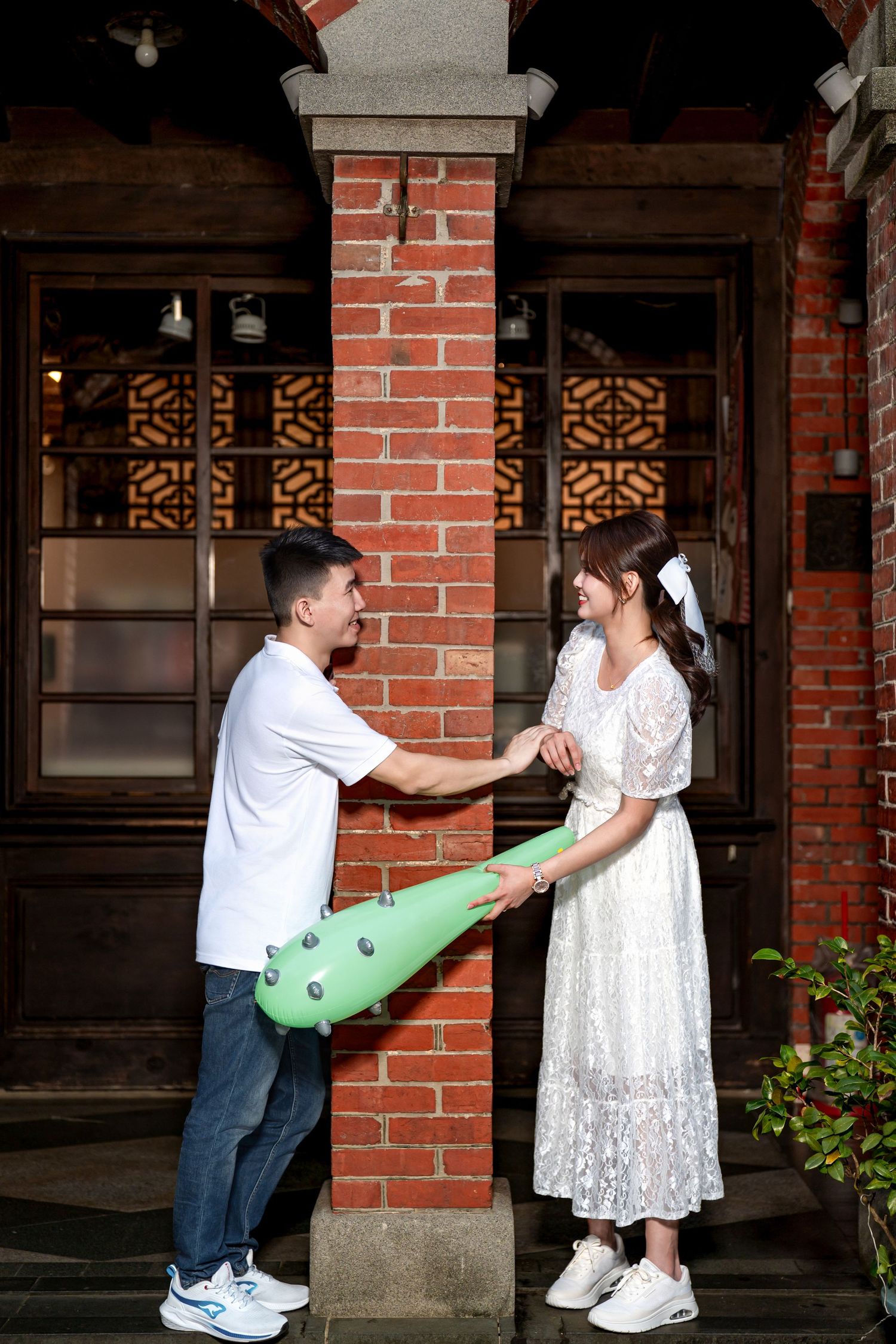 A playful sequence of photos showing a couple interacting with a green foam pool noodle against a brick building exterior.