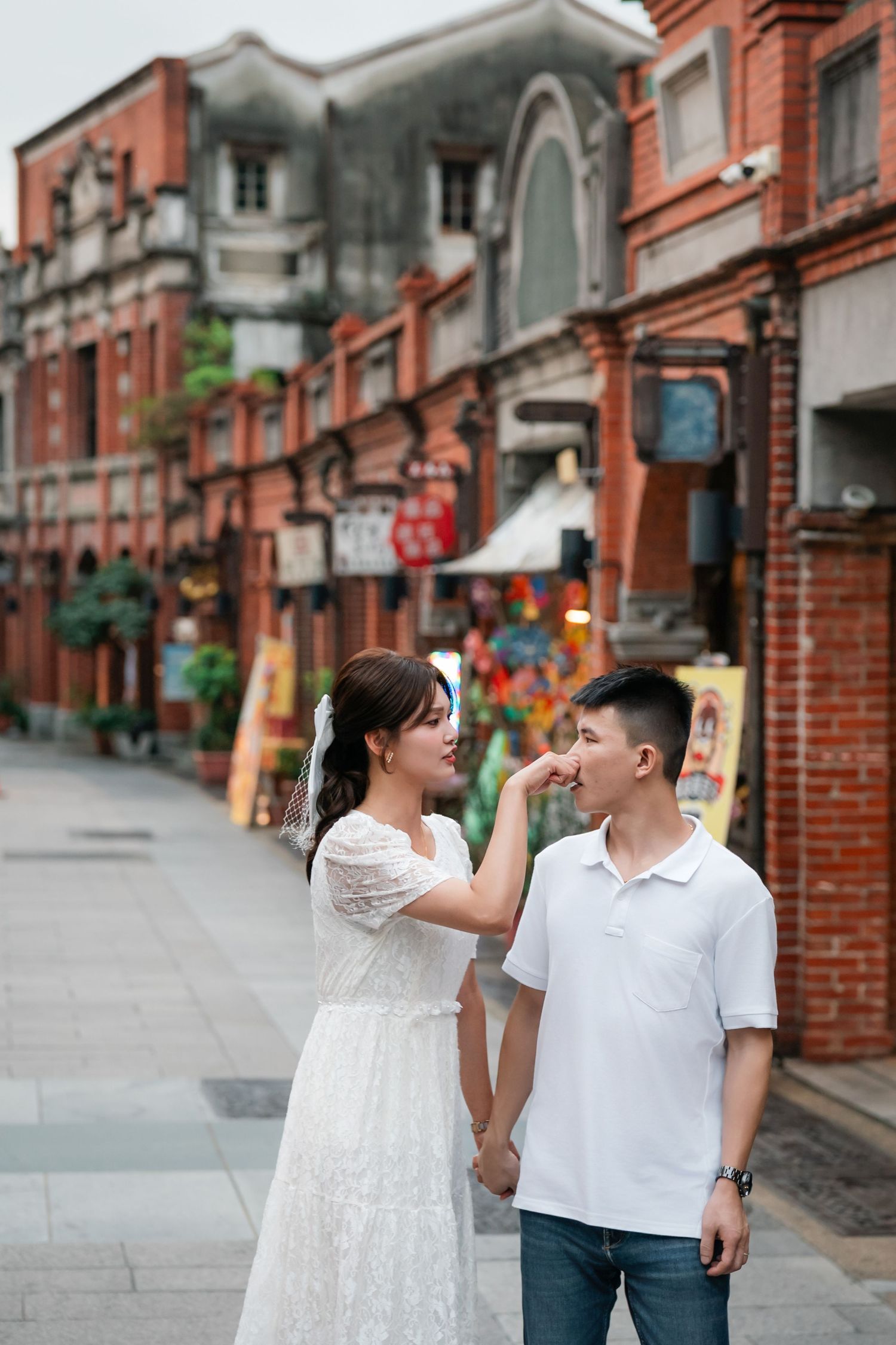 A couple shares playful moments along a traditional brick-lined street with red buildings in Taiwan.