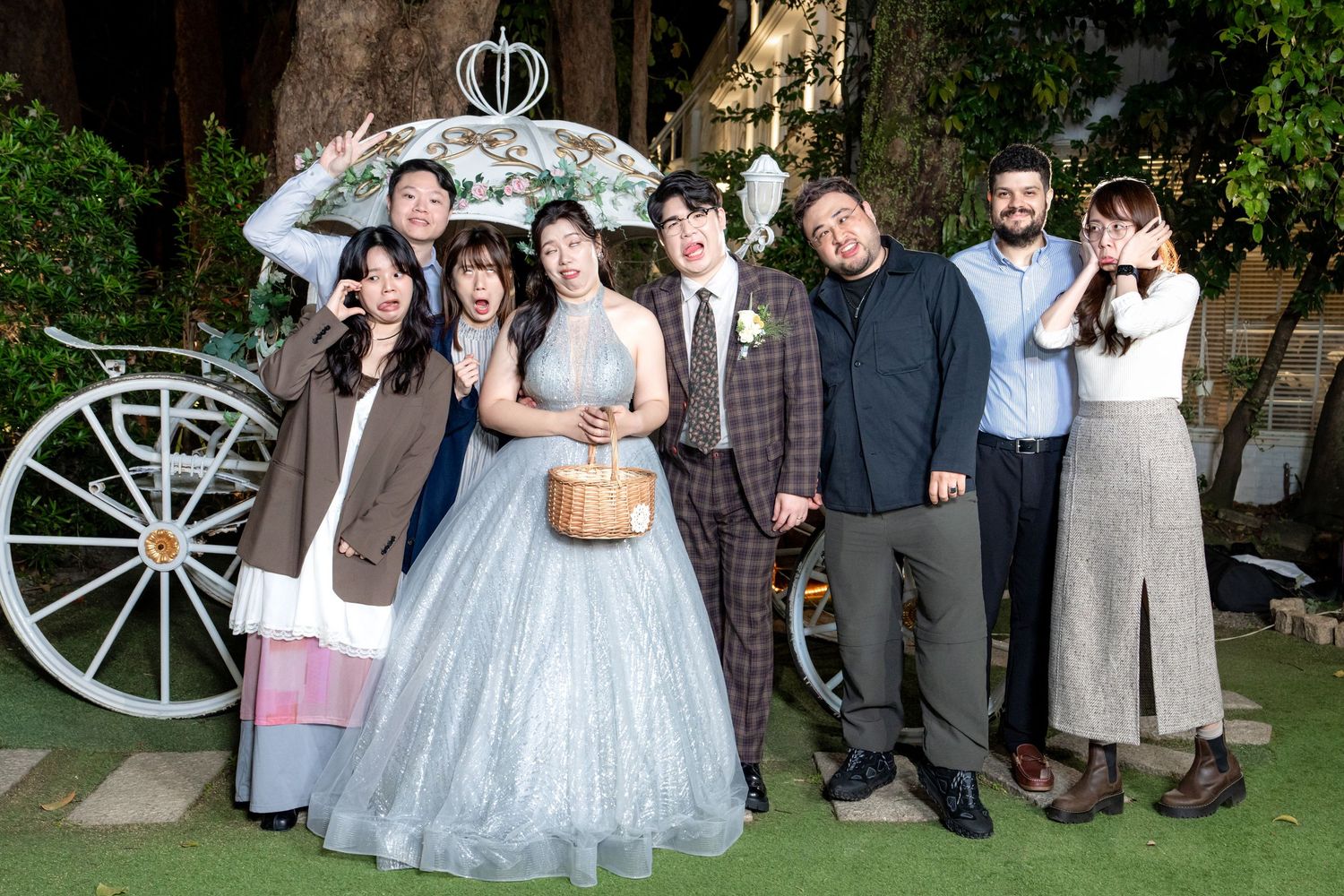 Wedding party poses together in front of white carriage wheel with bride wearing sparkly blue gown.