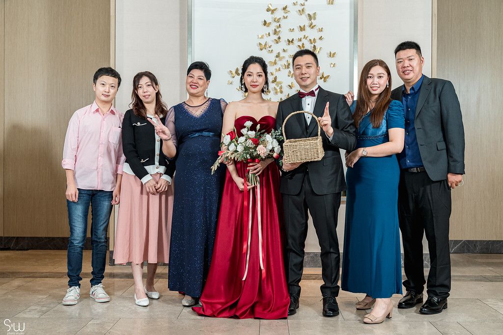 Wedding party group photo with couple in traditional red dress and formal attire.