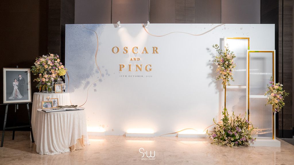 An elegant wedding reception backdrop features gold lettering, floral arrangements, and soft lighting.