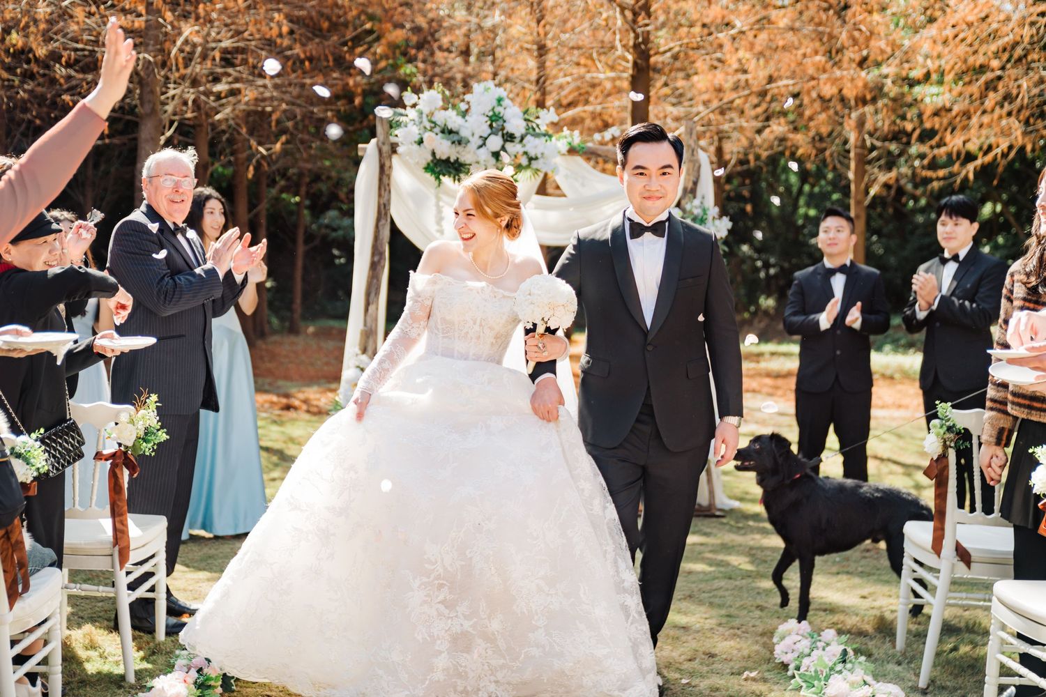 Wedding recessional in outdoor autumn setting with guests celebrating and white chairs.