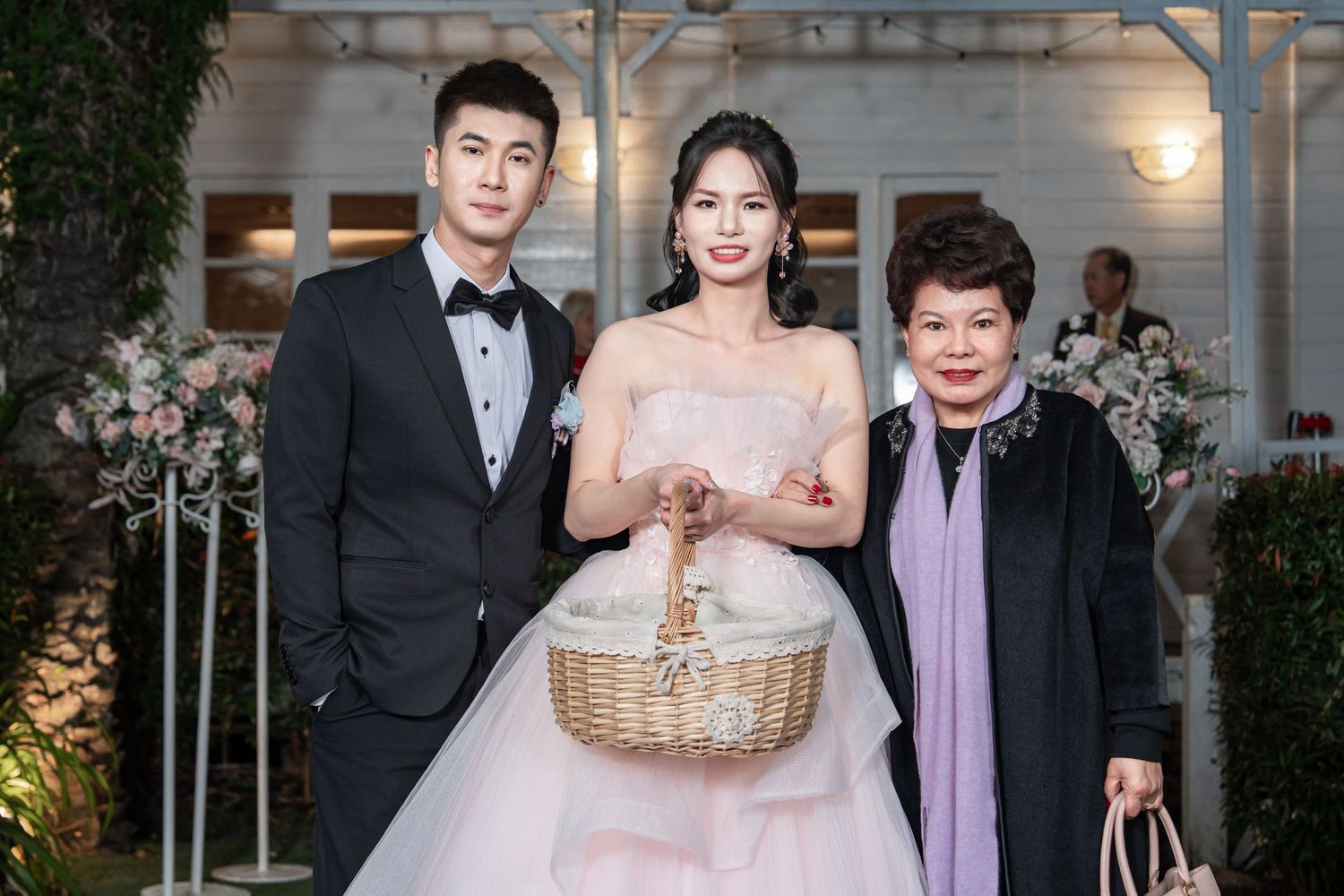 Wedding party poses with a wicker basket in front of an elegant venue entrance at dusk.