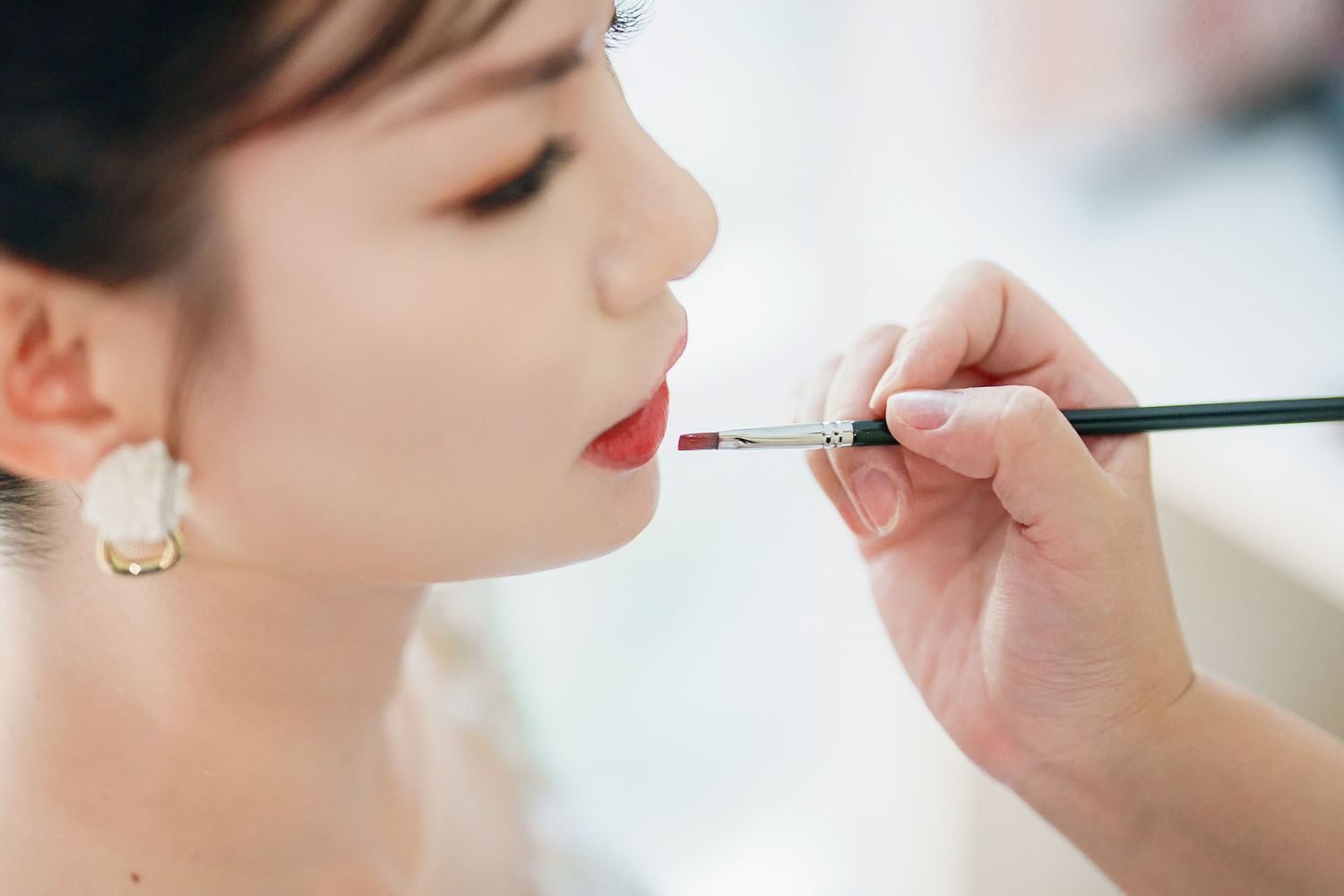 A makeup artist applies bright red lipstick during a professional beauty session.