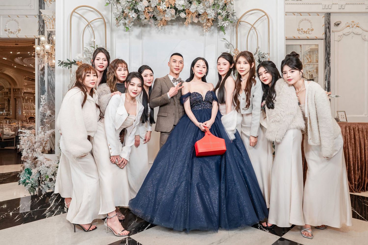 Group of bridesmaids in white dresses posing with two others in navy blue gowns at an elegant indoor venue.