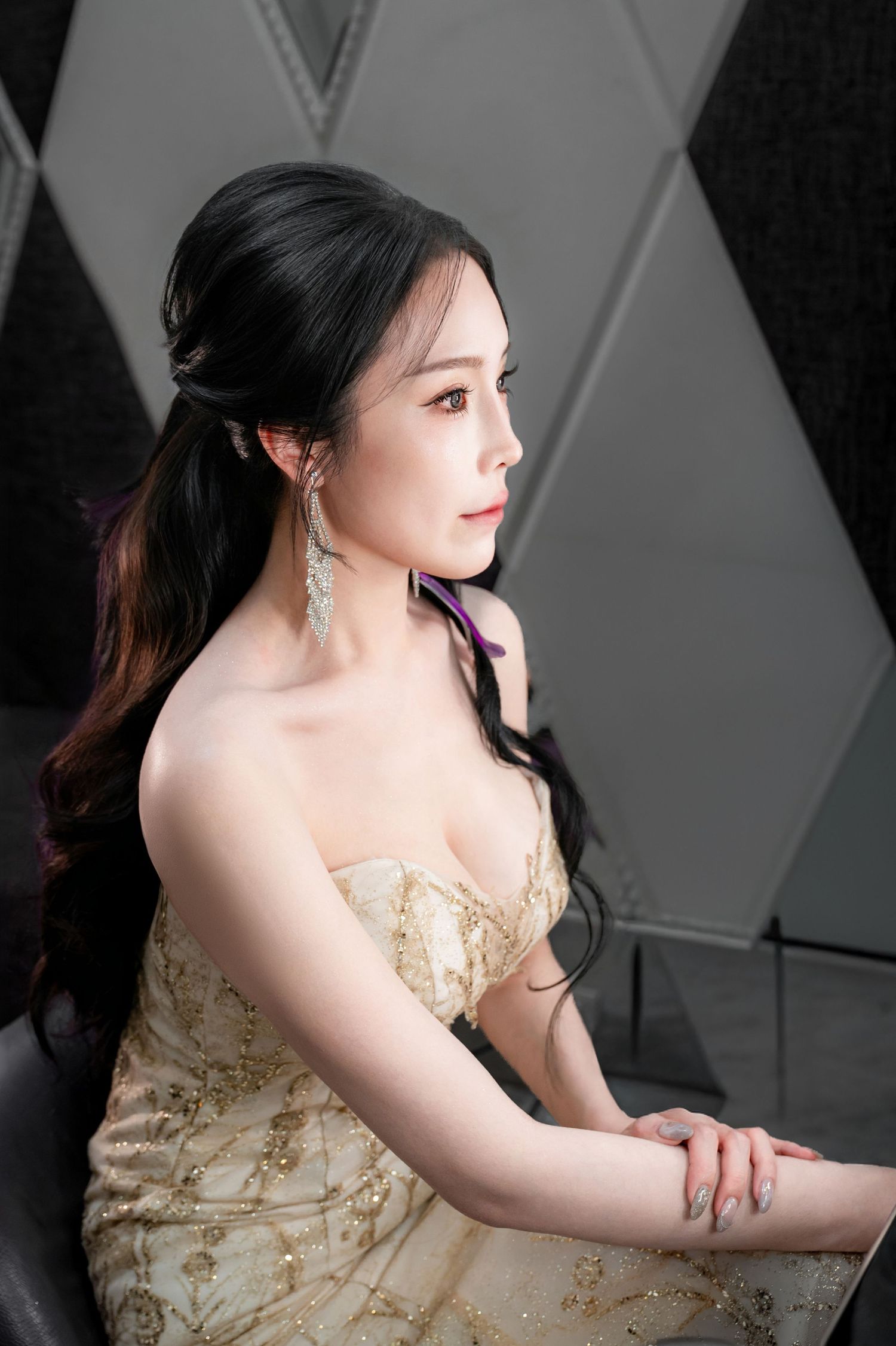 Side profile portrait of a woman in an elegant gold embroidered strapless gown with dangling earrings and dark hair.
