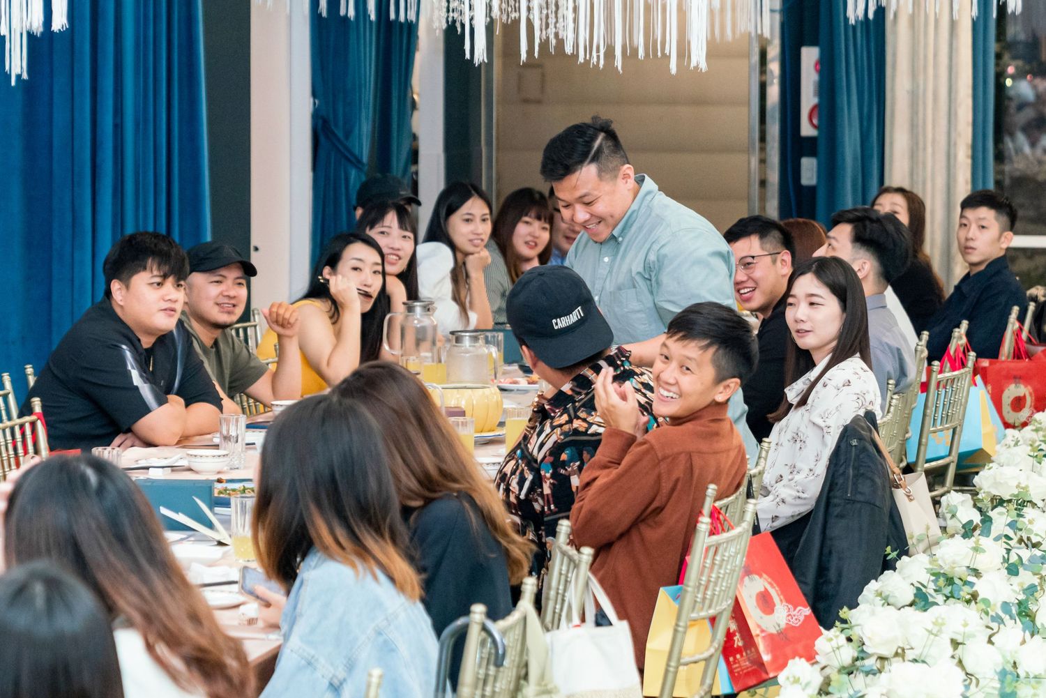 A group of young people gathered around a long table for a social dining event with blue decorative elements.