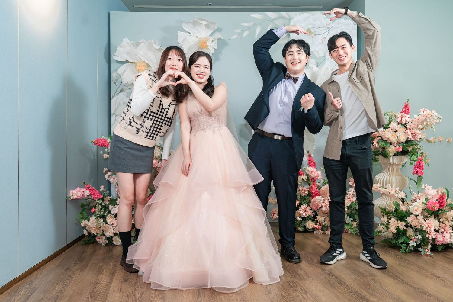 Children pose together in formal attire against a blue wall decorated with pink floral arrangements.