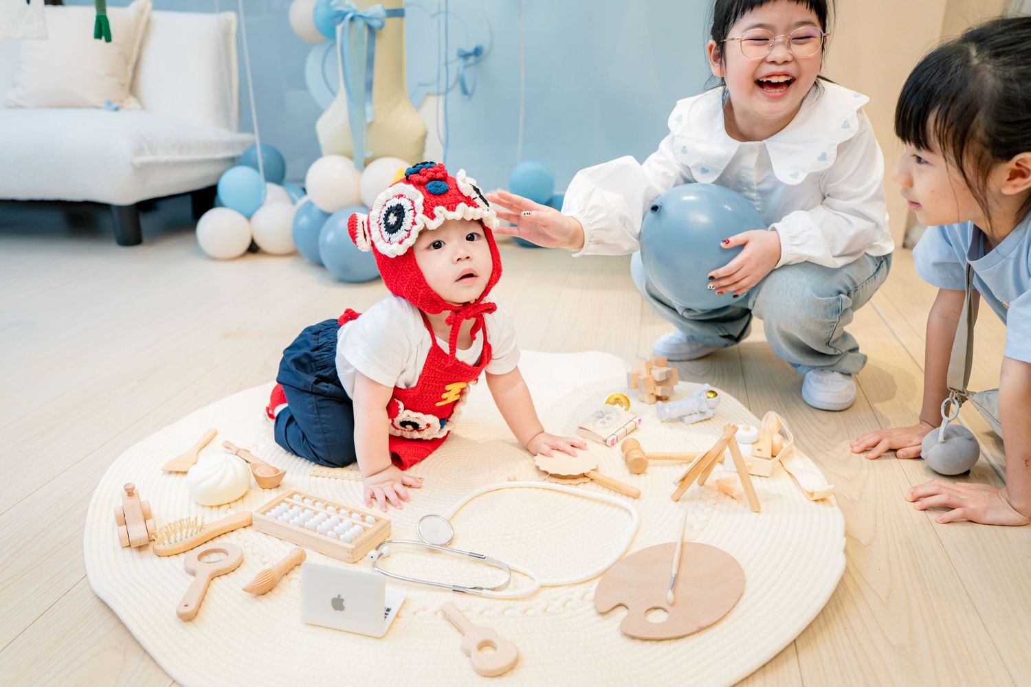 Children sit on the floor playing with colorful toys and educational materials in a bright classroom setting.