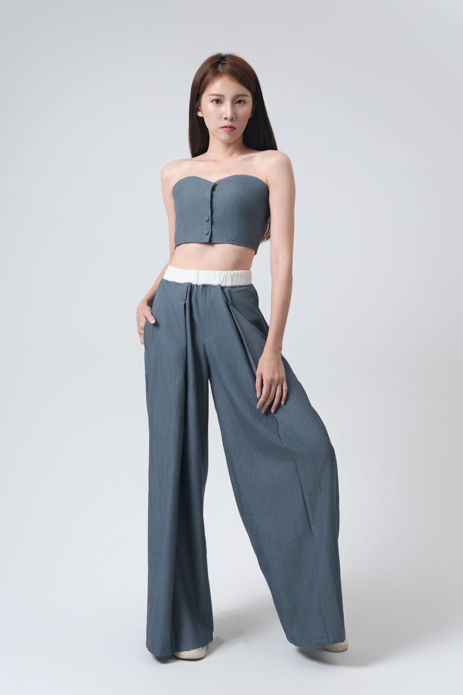 Model wearing wide-leg palazzo pants in slate gray color with strapless top against white background.