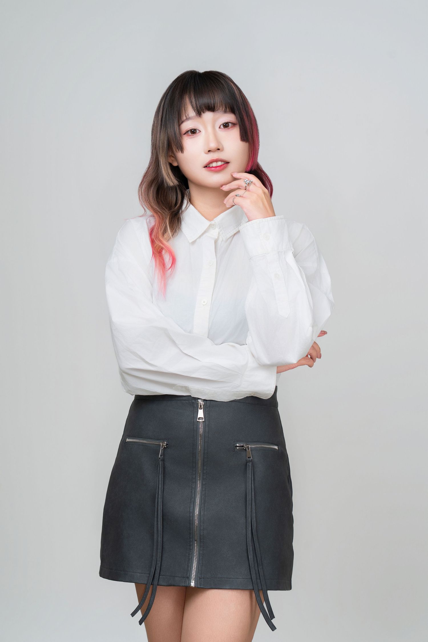 A person in a white button-down shirt and black mini skirt with zipper details poses against a light gray background.