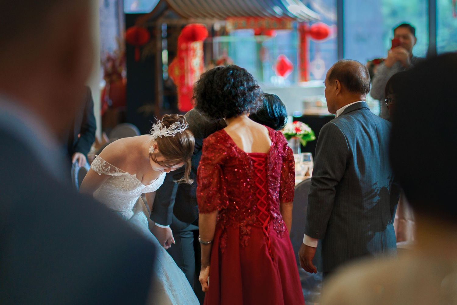 A couple shares a romantic dance at a wedding reception with red decor and guests in the background.