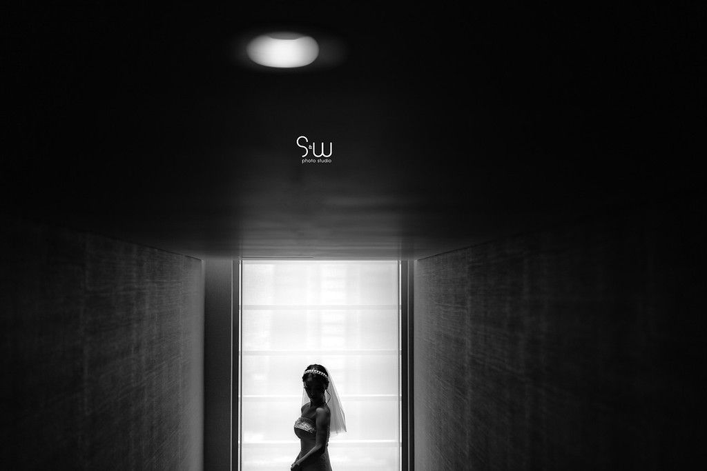 A silhouetted figure stands in a doorway under dramatic lighting in black and white photography.