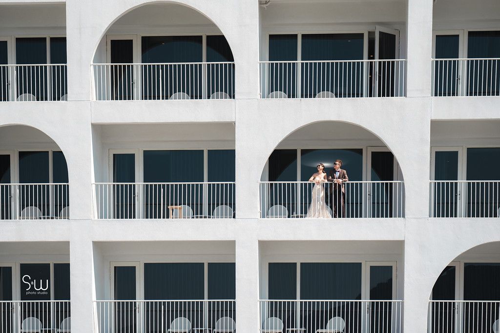Romantic wedding portrait captured through arched balconies of a white Mediterranean building.