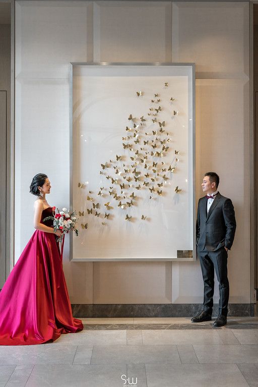 Elegant wedding portrait with couple standing on opposite sides of golden butterfly wall art.