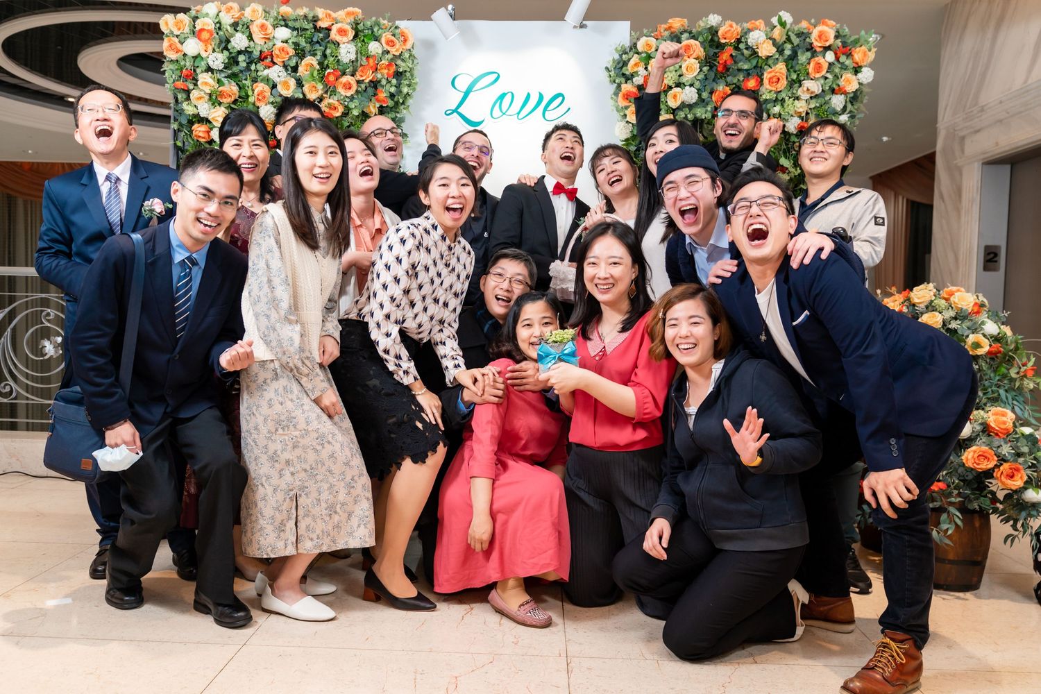 Cheerful group photo with people making fun poses in front of peach floral decorations.