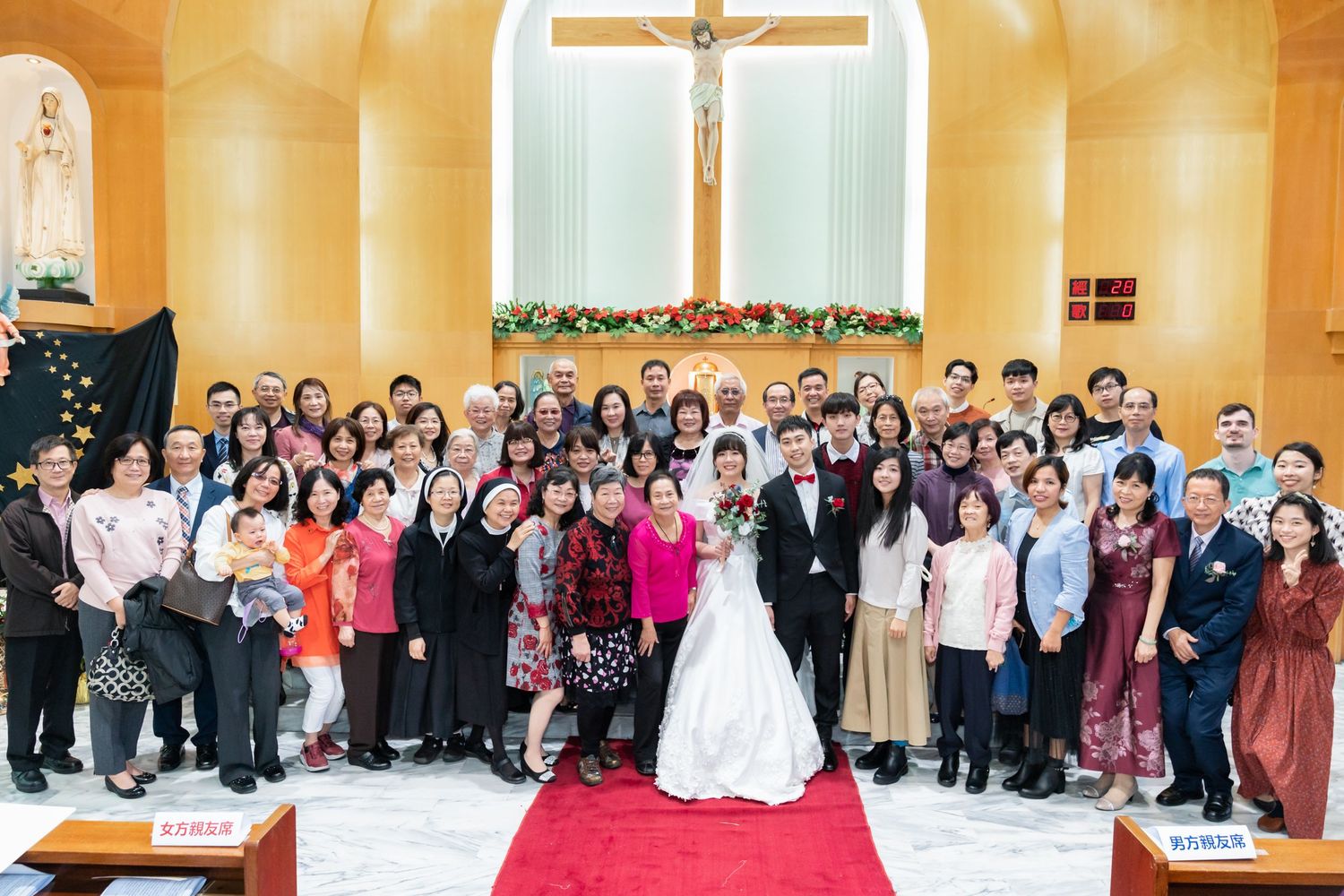 Large wedding group photo inside a church with yellow walls and a crucifix backdrop.